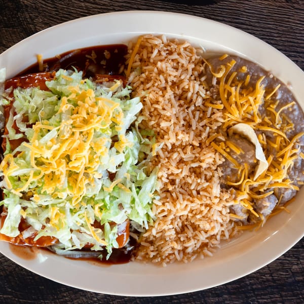 Adalbertacos Mexican Food enchiladas with rice, beans, shredded lettuce, and cheese on a white plate.