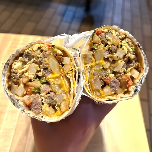 A hand holds a large Adalbertacos Mexican Food burrito, cut in half, revealing a cheesy, meaty filling.