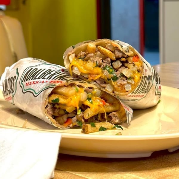 Two halves of a large Adalbertacos Mexican Food burrito, filled with meat, fries, and melted cheese.