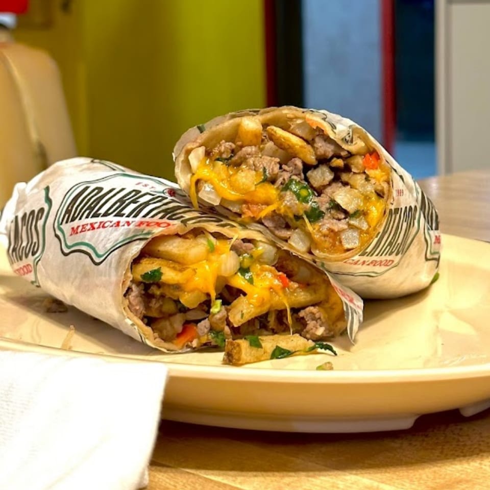 Two halves of a large Adalbertacos Mexican Food burrito, filled with meat, fries, and melted cheese.