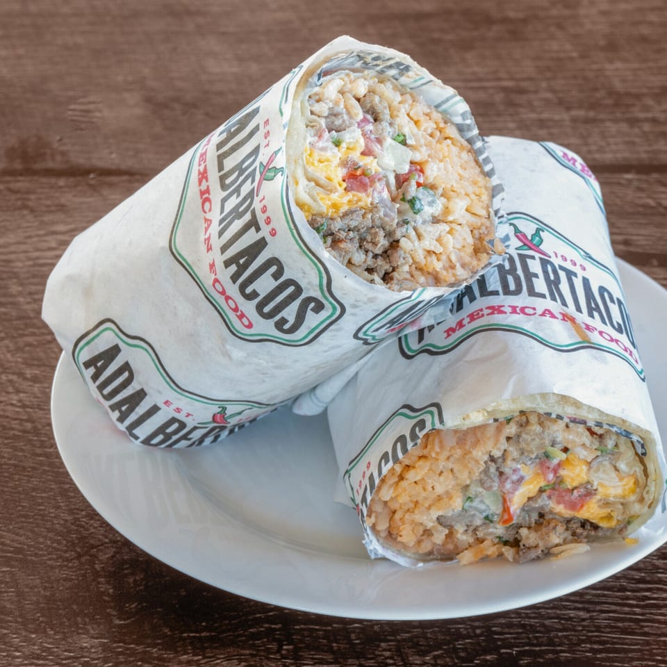 Two Adalbertacos Mexican Food burritos, unwrapped to show rice, meat, cheese, and salsa, on a white plate.