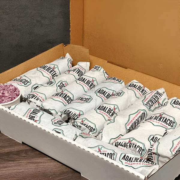 A catering box filled with individually wrapped burritos from Adalbertacos, with a side of red onions.