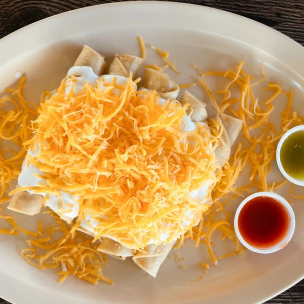 Adalbertacos Mexican Food's taquitos topped with sour cream and shredded cheddar cheese, with two salsa cups.