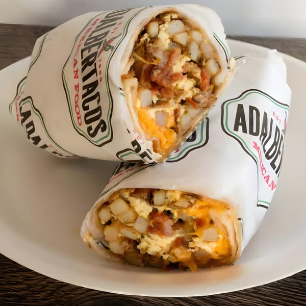 Two Adalbertacos burritos, filled with eggs, cheese, and potatoes, on a white plate.