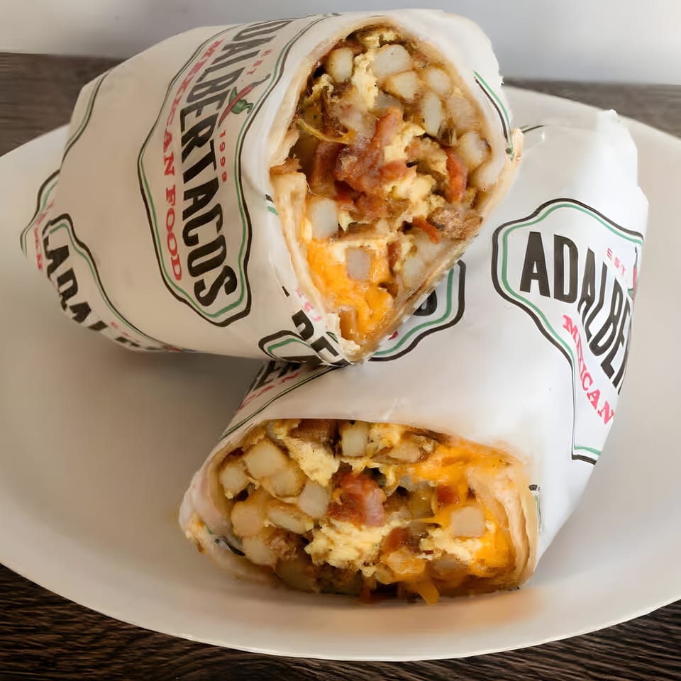 Two Adalbertacos burritos, filled with eggs, cheese, and potatoes, on a white plate.