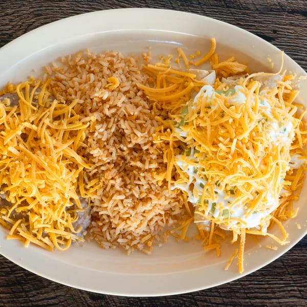 Adalbertacos Mexican Food plate with rice, shredded cheese, and sour cream on a white plate.