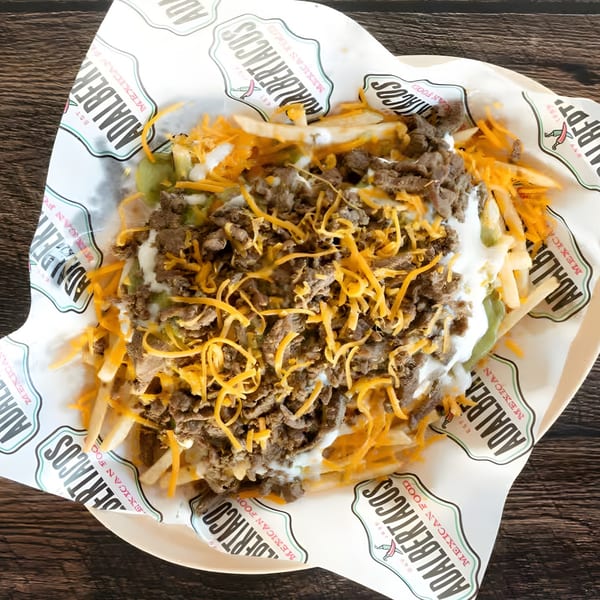 Adalbertacos carne asada fries topped with cheese, sour cream, and guacamole in a branded wrapper.