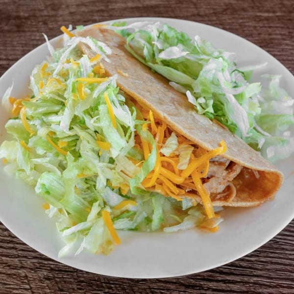 A crispy Adalbertacos Mexican Food taco filled with shredded chicken, cheese, and lettuce on a white plate.
