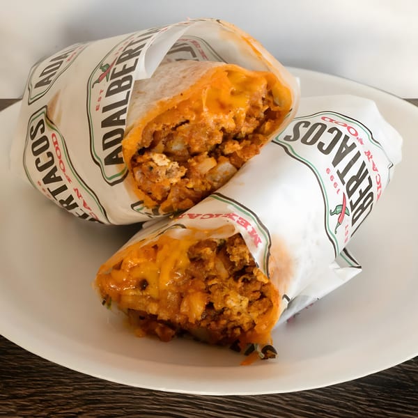 Two Adalbertacos burritos, cut in half, revealing a cheesy, meaty filling, on a white plate.