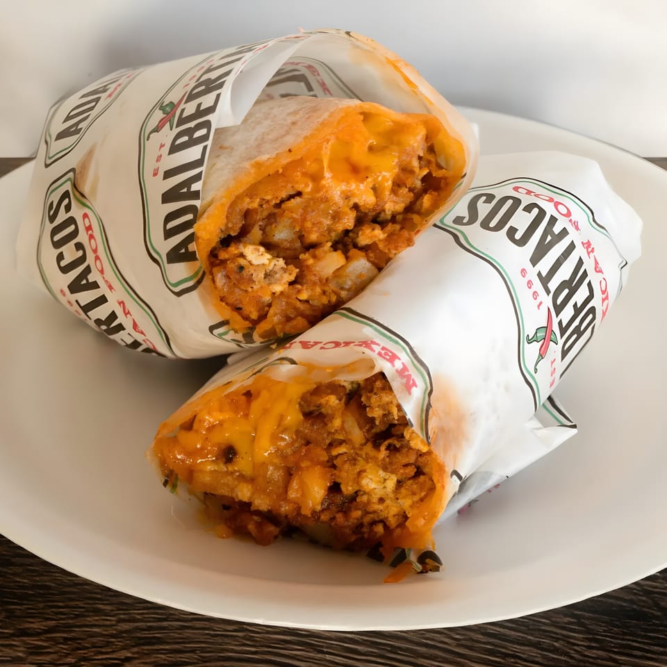 Two Adalbertacos burritos, cut in half, revealing a cheesy, savory filling, on a white plate.