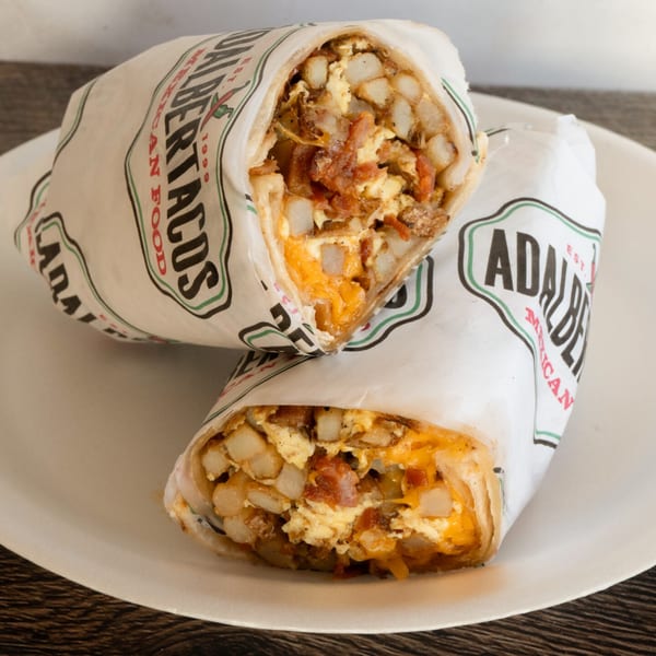 Two Adalbertacos Mexican Food burritos, filled with potatoes, eggs, and cheese, on a white plate.